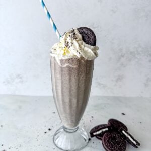 Tall glass filled with cookies and cream milkshake topped with whipped cream and an Oreo cookie.