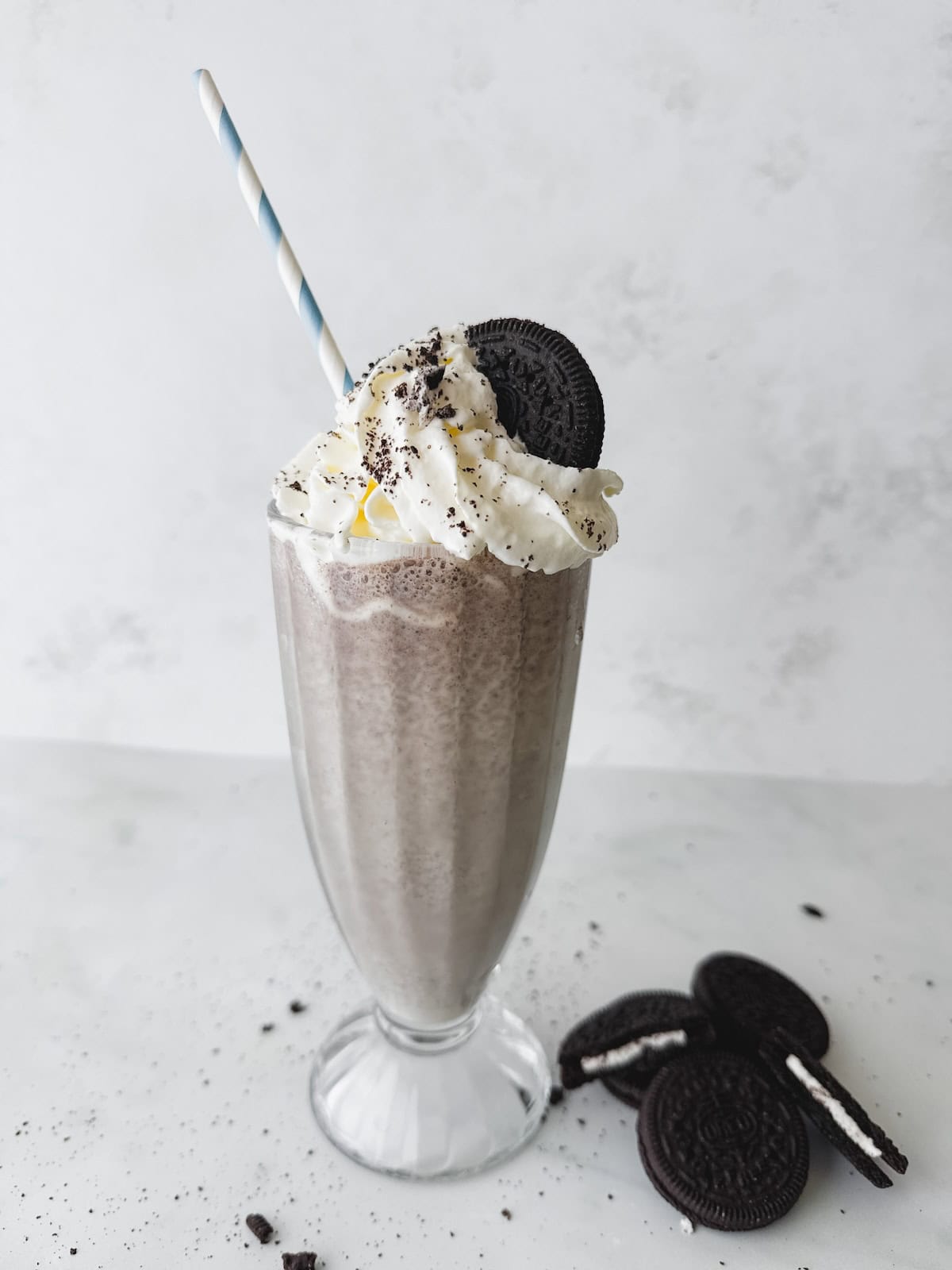 Tall glass filled with cookies n cream milkshake topped with whipped cream and an Oreo cookie.