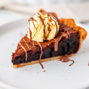 A slice of gluten free brownie pie on a white plate, topped with vanilla ice cream.