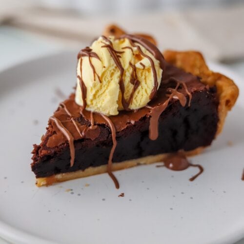 A slice of gluten free brownie pie on a white plate, topped with vanilla ice cream.