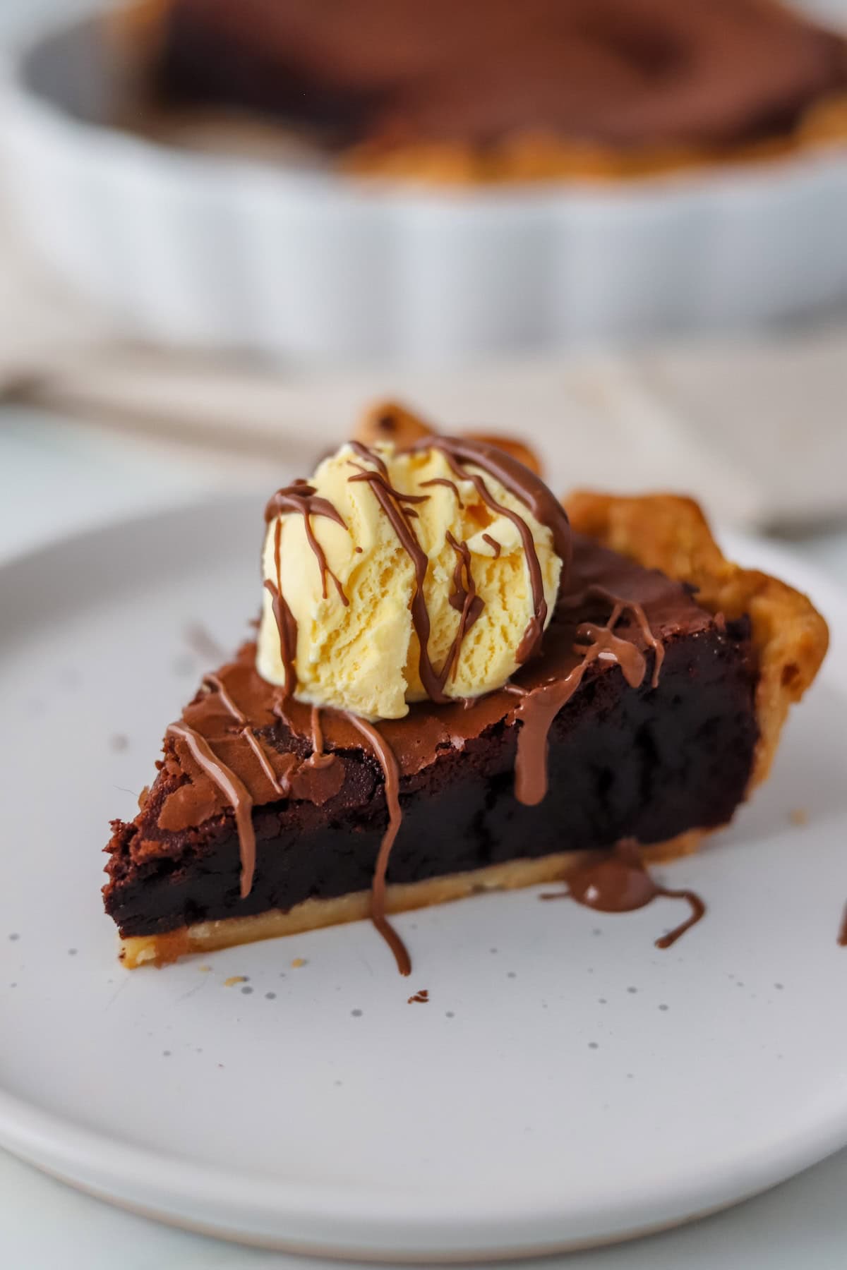 A slice of gluten free brownie pie on a white plate, topped with vanilla ice cream.