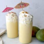 Two tall glasses filled with mango milkshake and topped with whipped cream and a tiny umbrella.