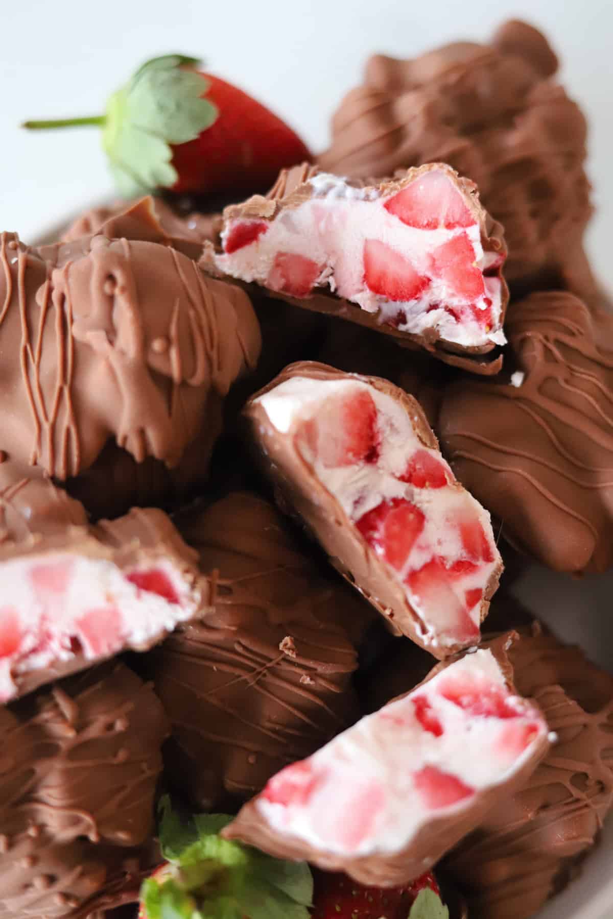 Chocolate strawberry yogurt clusters on a plate with some sliced in half to reveal the filling.