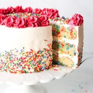 Gluten free funfetti cake on a white cake stand with a slice being removed.
