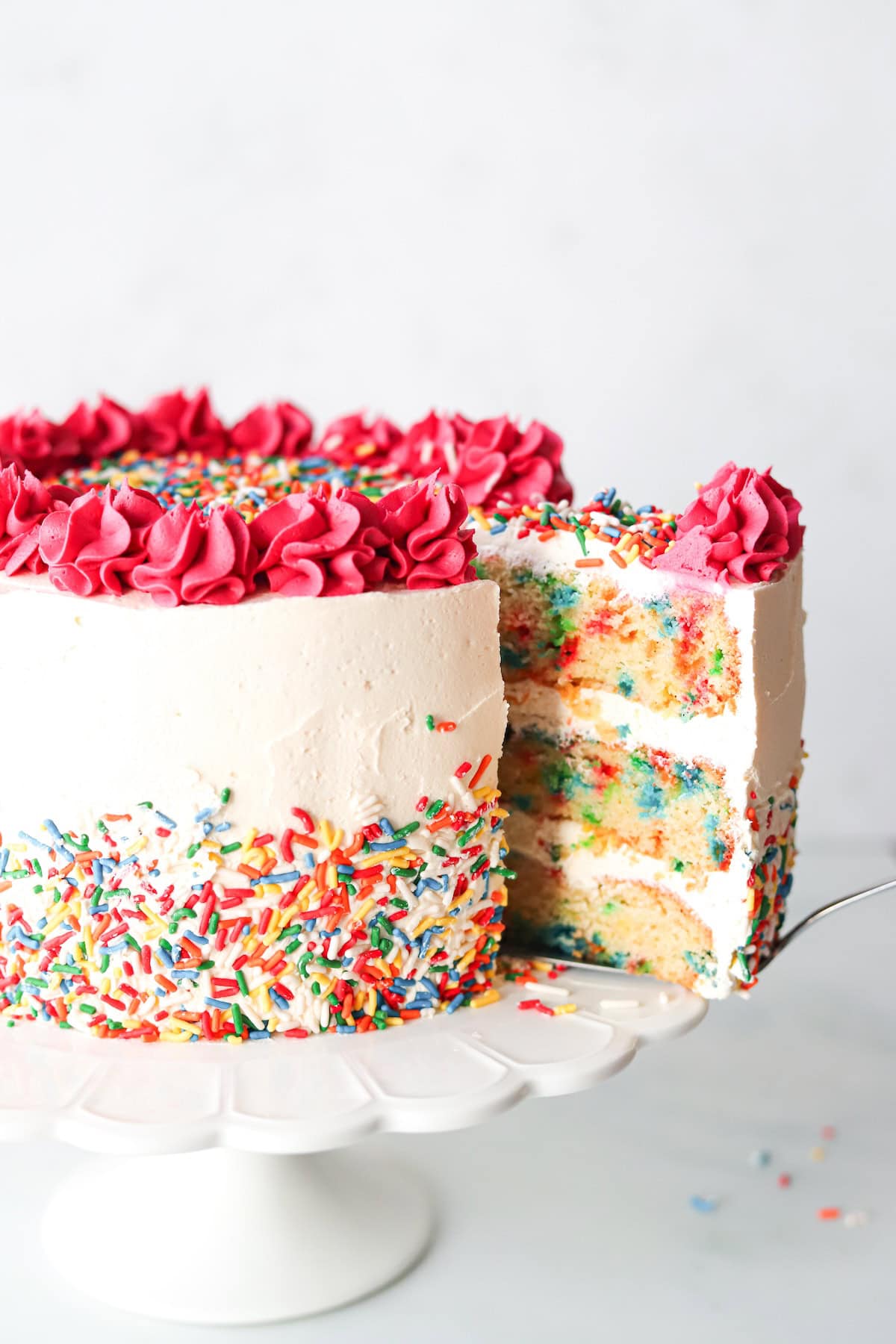 Gluten free funfetti cake on a white cake stand with a slice being removed.