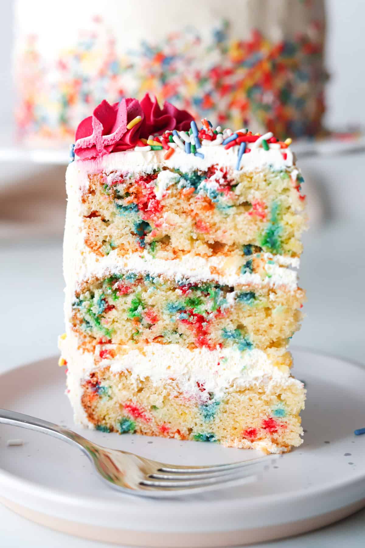 A slice of gluten free funfetti cake on a white plate with a fork.