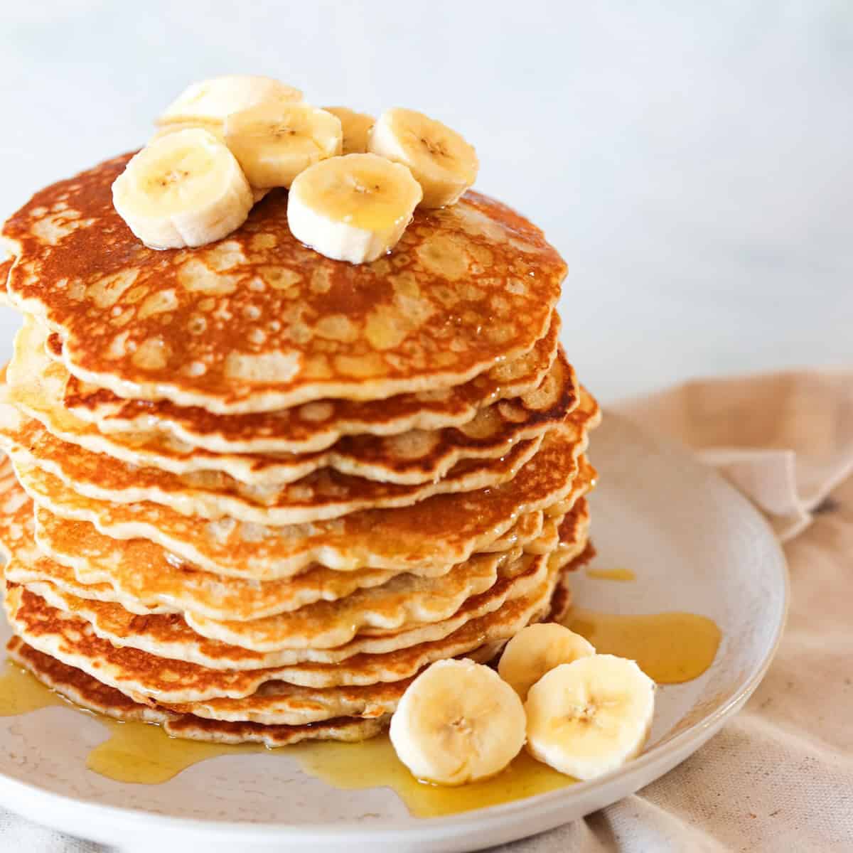 Gluten free banana pancakes stacked on a white plate, topped with sliced bananas.