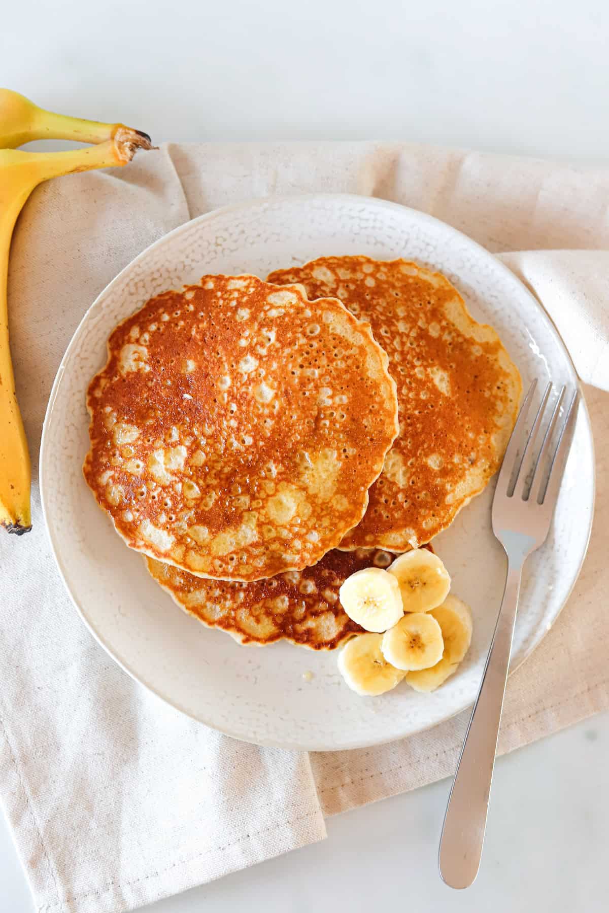 Three gluten free banana pancakes on a plate with a fork.