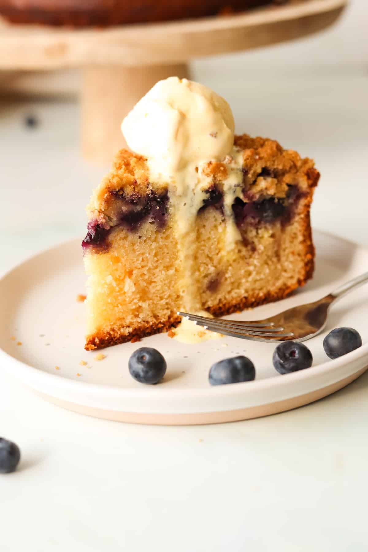 A slice of gluten free blueberry crumb cake on a white plate topped with ice cream.