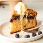 A slice of gluten free blueberry crumb cake on a white plate topped with ice cream.