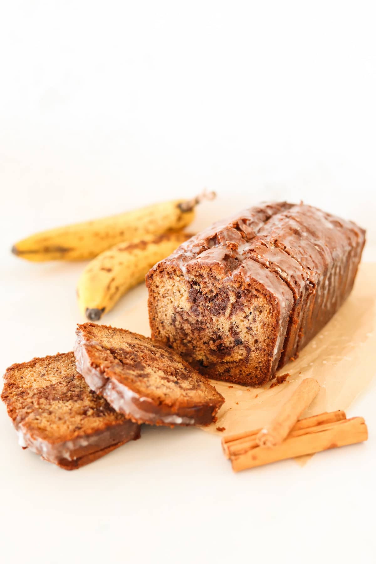 Cinnamon swirl banana bread on a white surface with ripe bananas in the background.