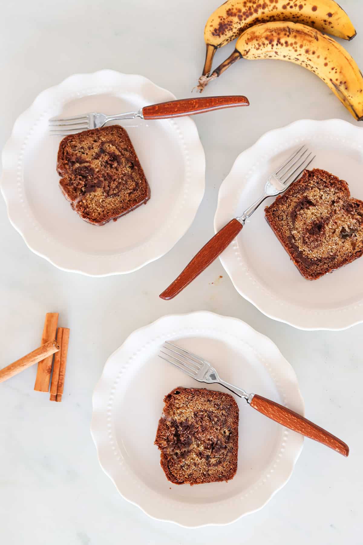 Three slices of gluten free cinnamon swirl banana bread on white plates with forks.