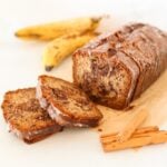 Cinnamon swirl banana bread on a white surface with ripe bananas in the background.