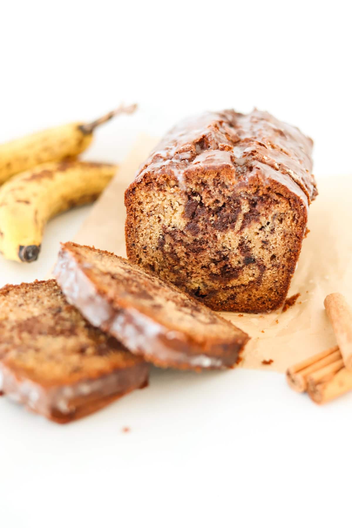 Sliced cinnamon swirl banana bread on a white surface with ripe bananas in the background.