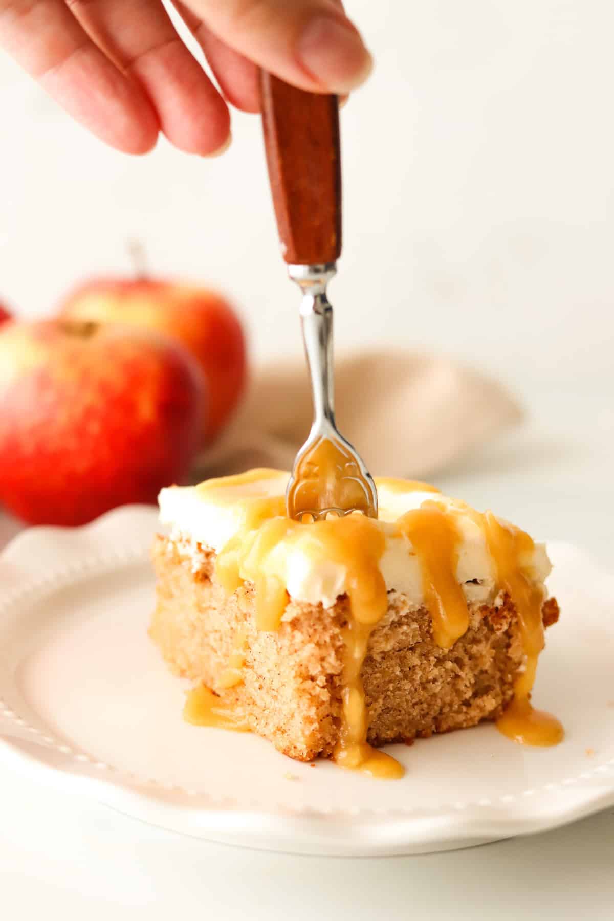 A slice of caramel apple cake on a white plate with a fork.