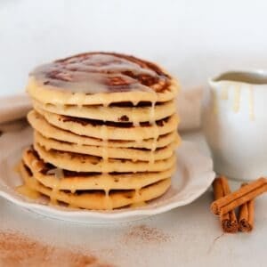 A stack of cinnamon swirl pancakes drizzled with cream cheese frosting.