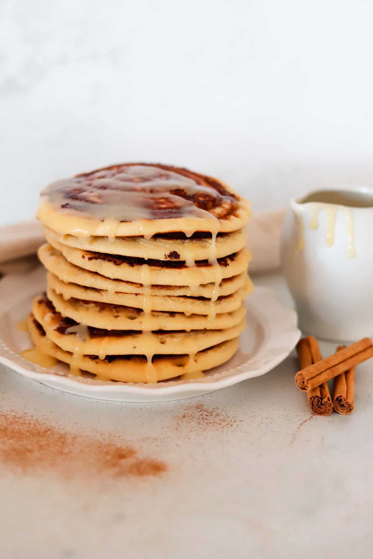 A stack of cinnamon swirl pancakes drizzled with cream cheese frosting.