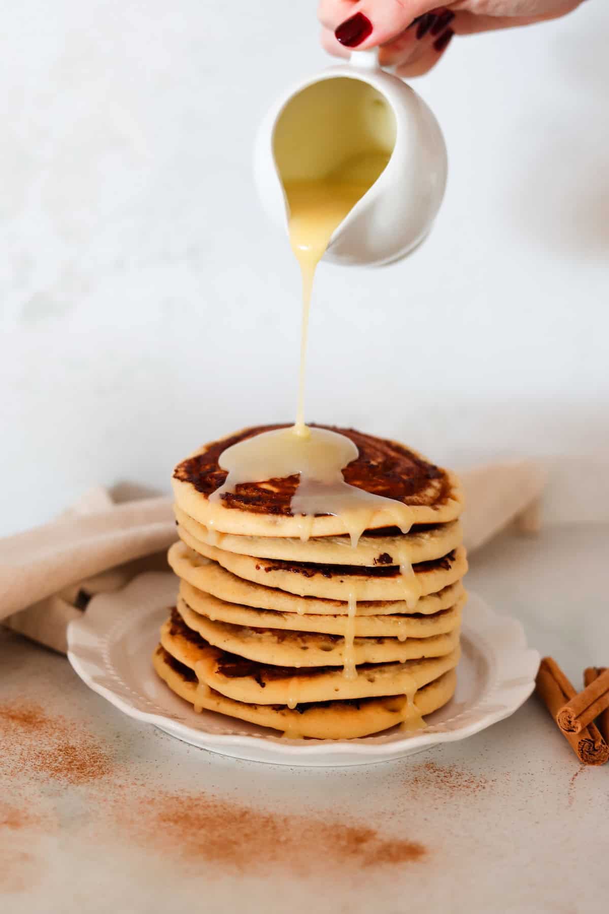 Cream cheese frosting is being poured over a stack of cinnamon swirl pancakes.